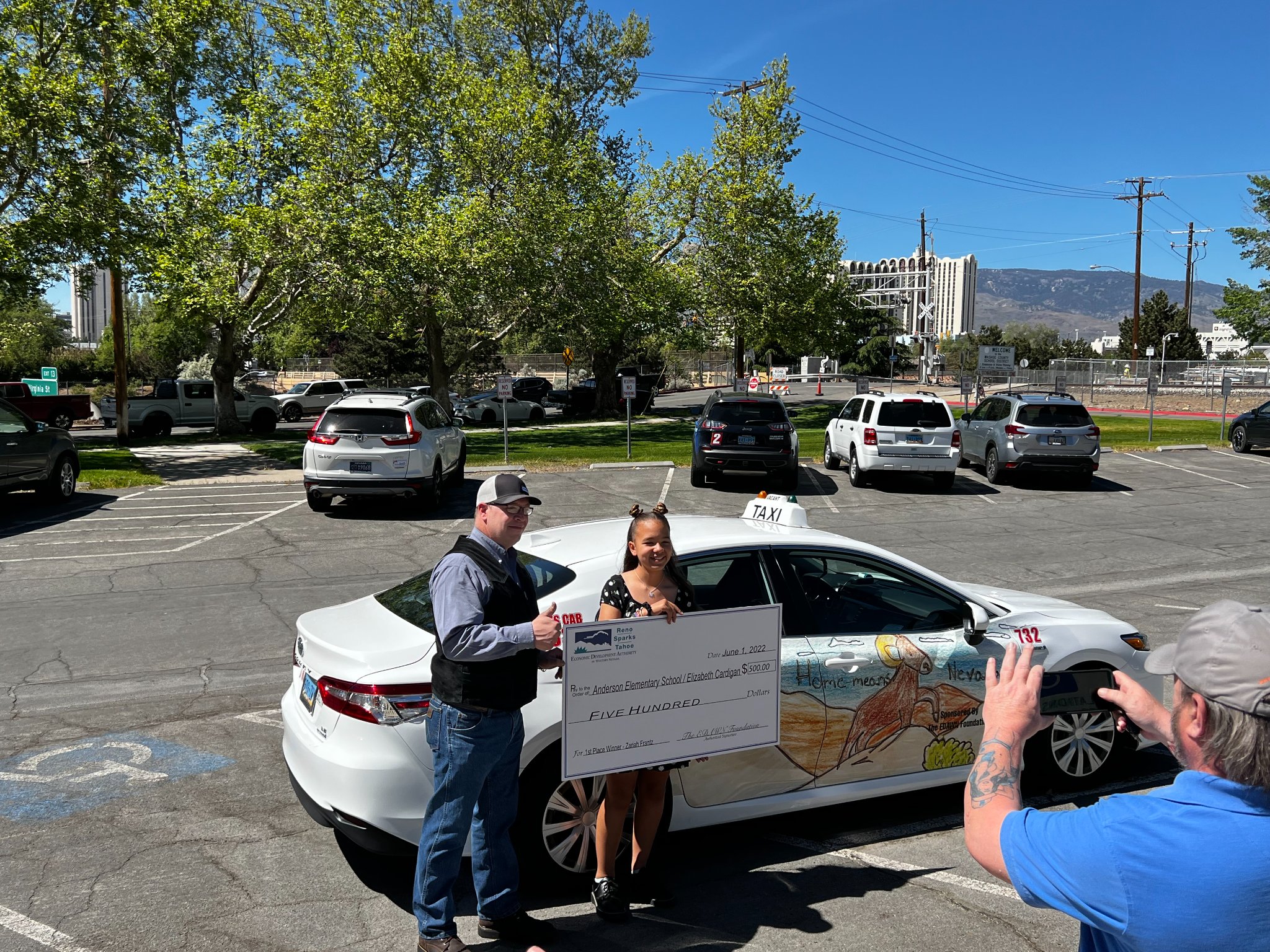inline image showing a reno taxi with a new design and the winner of the design receiving a prize